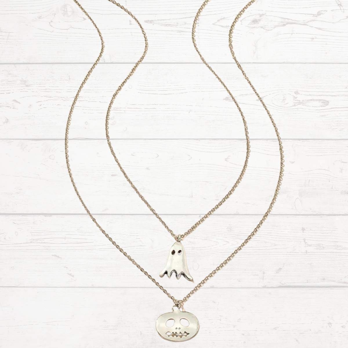 Silver pendant necklace with ghost and jack-o-lantern charms on linked chains.