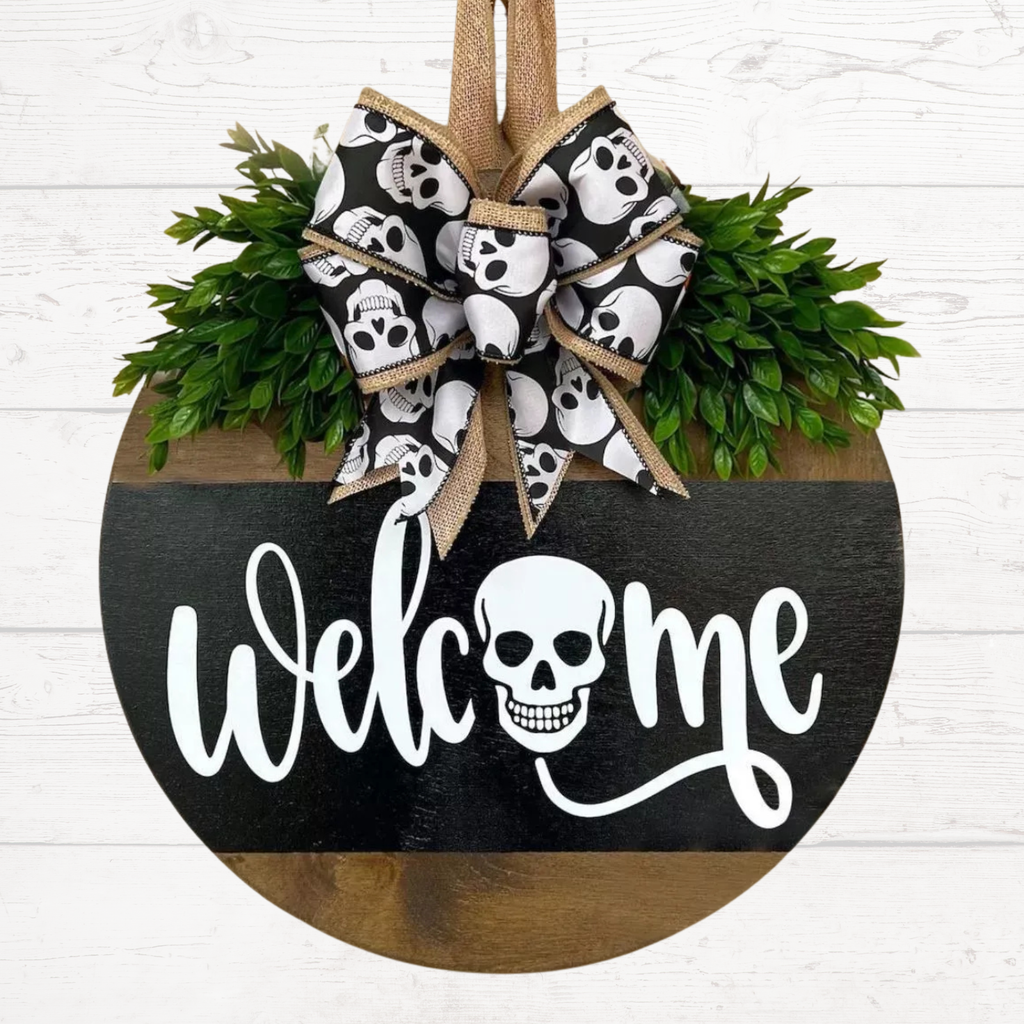 Halloween door hanger with burlap bow, skulls, and “Welcome Me” text on black sign.