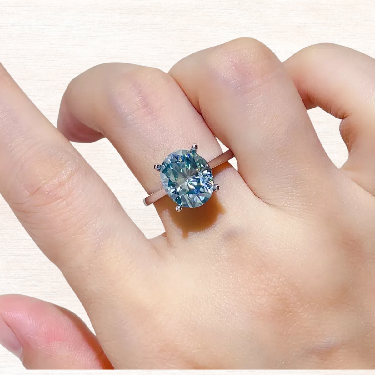 Blue moissanite studded ring on hand, silver band with four-prong center stone