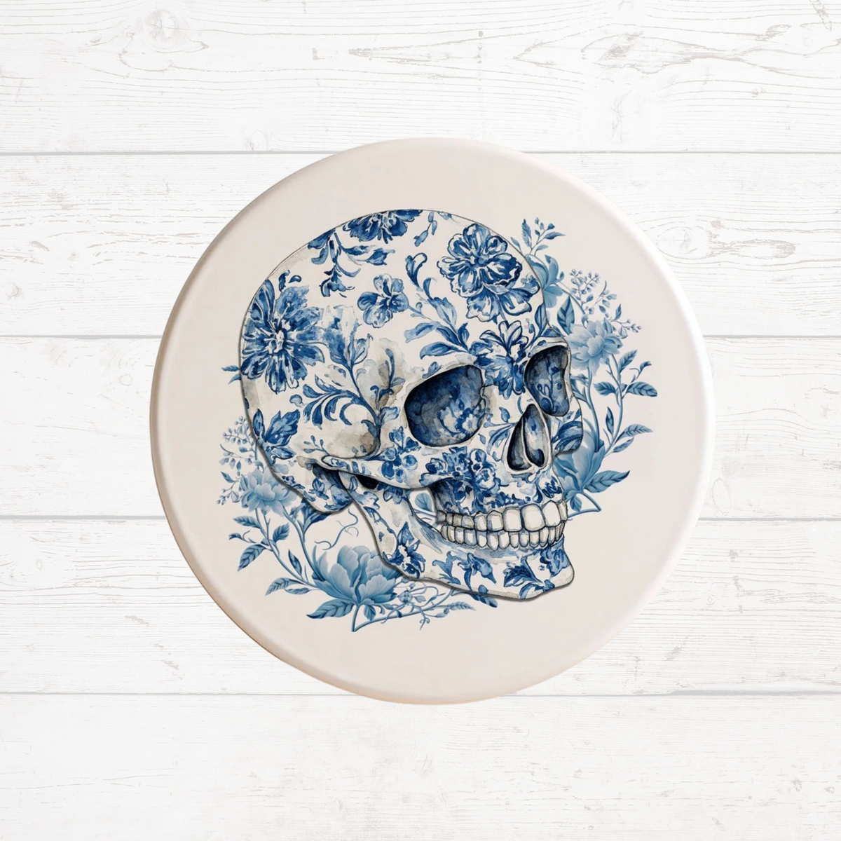 Blue-and-white skull coaster surrounded by floral vines on a white round base