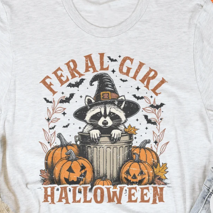Light heather gray tee close-up of raccoon witch hat Halloween graphic and “FERAL-GIRL”