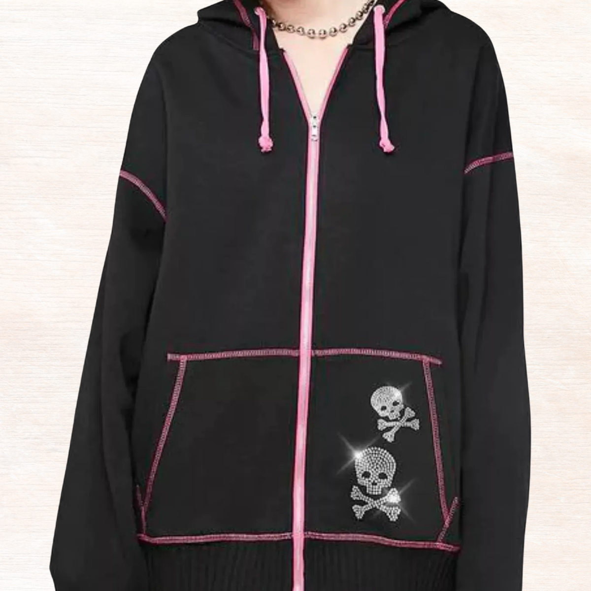 Black zip-up drawstring hoodie with pink zipper and skull graphic on chest pocket.